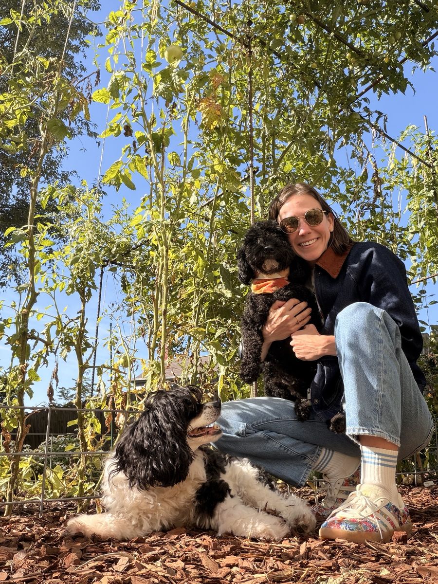 Haley crouching under tall tomato plants, hugging Wes, with Colt lying in the mulch beside her