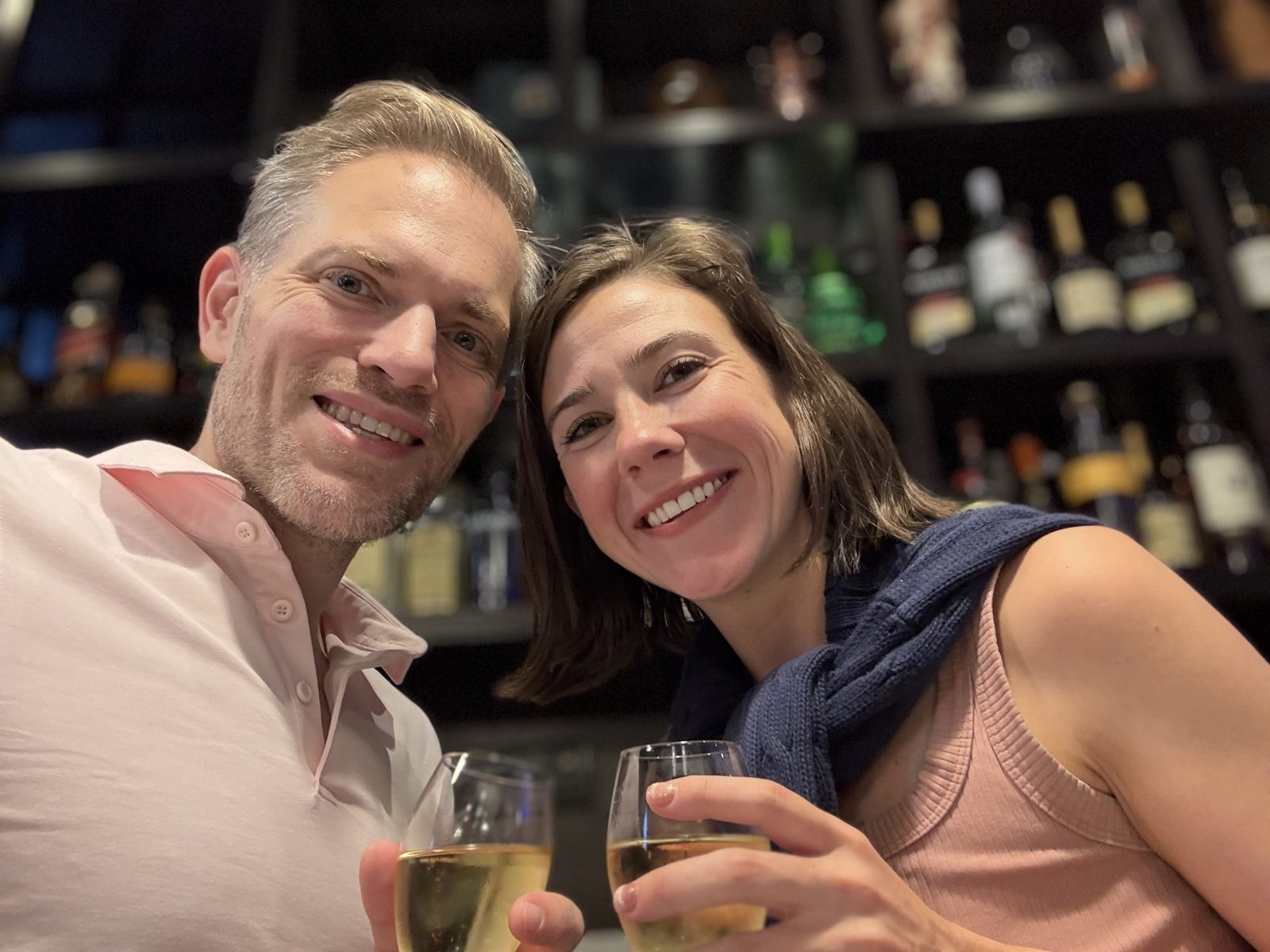 Haley and Michael in a selfie at a bar, each holding a glass of white wine