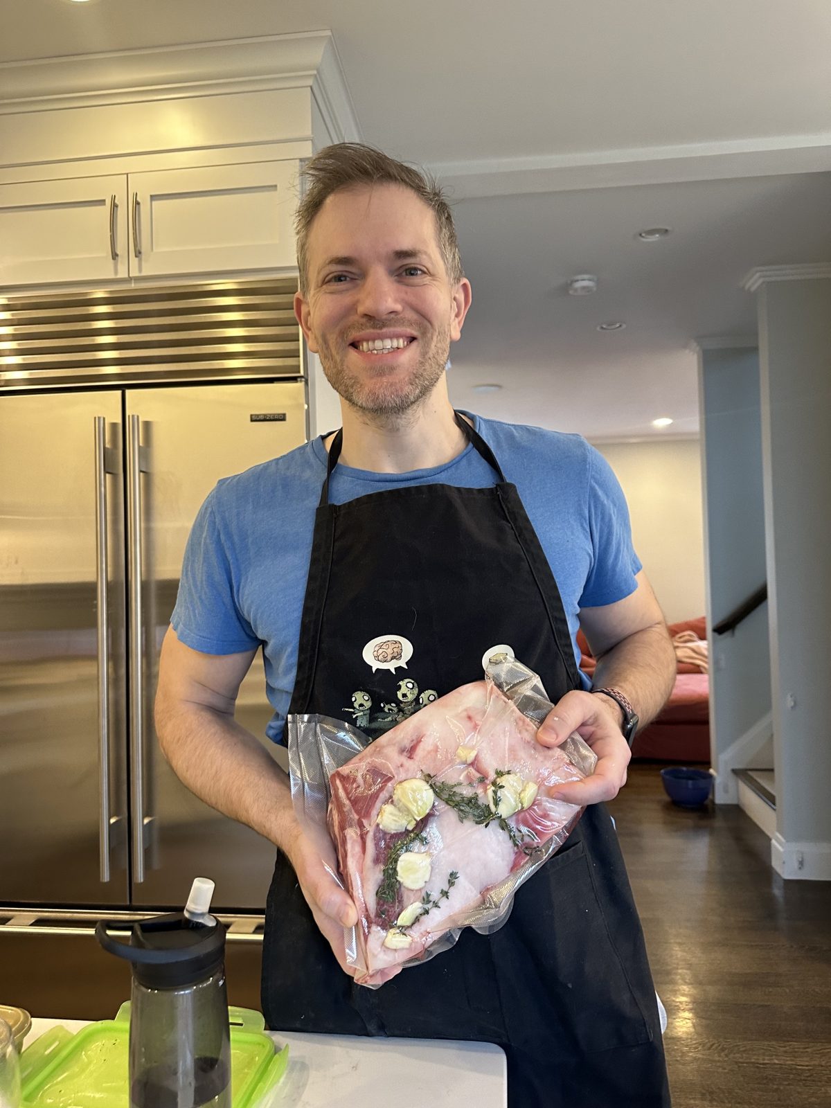 Michael in an apron holding a vacuum-sealed cut of meat with garlic and thyme