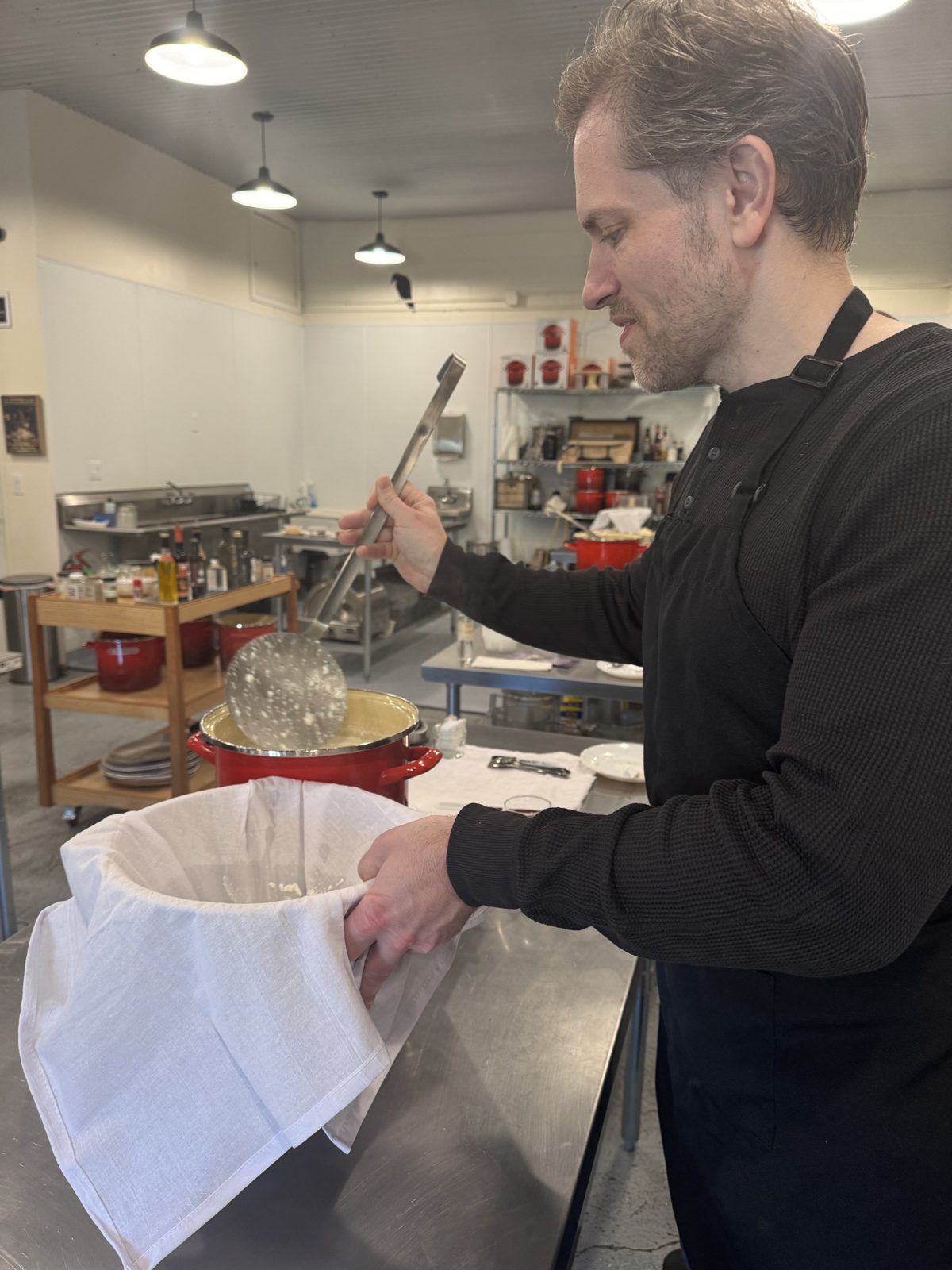 Michael in an apron ladling curds into a cloth-lined bowl in a teaching kitchen