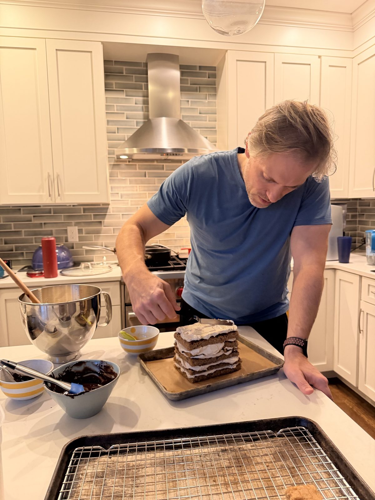 Michael frosting a tall stacked layer cake at the kitchen island