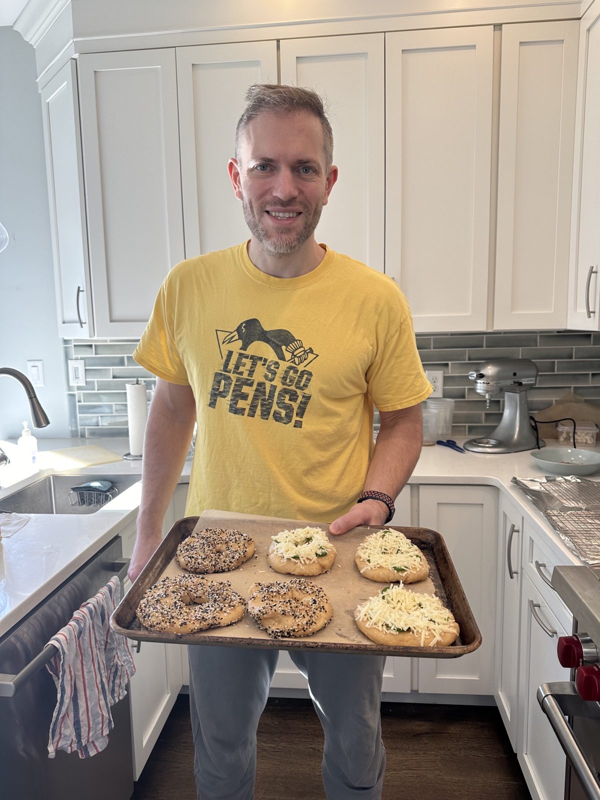 Michael in a Let's Go Pens shirt holding a tray of homemade everything and cheese bagels