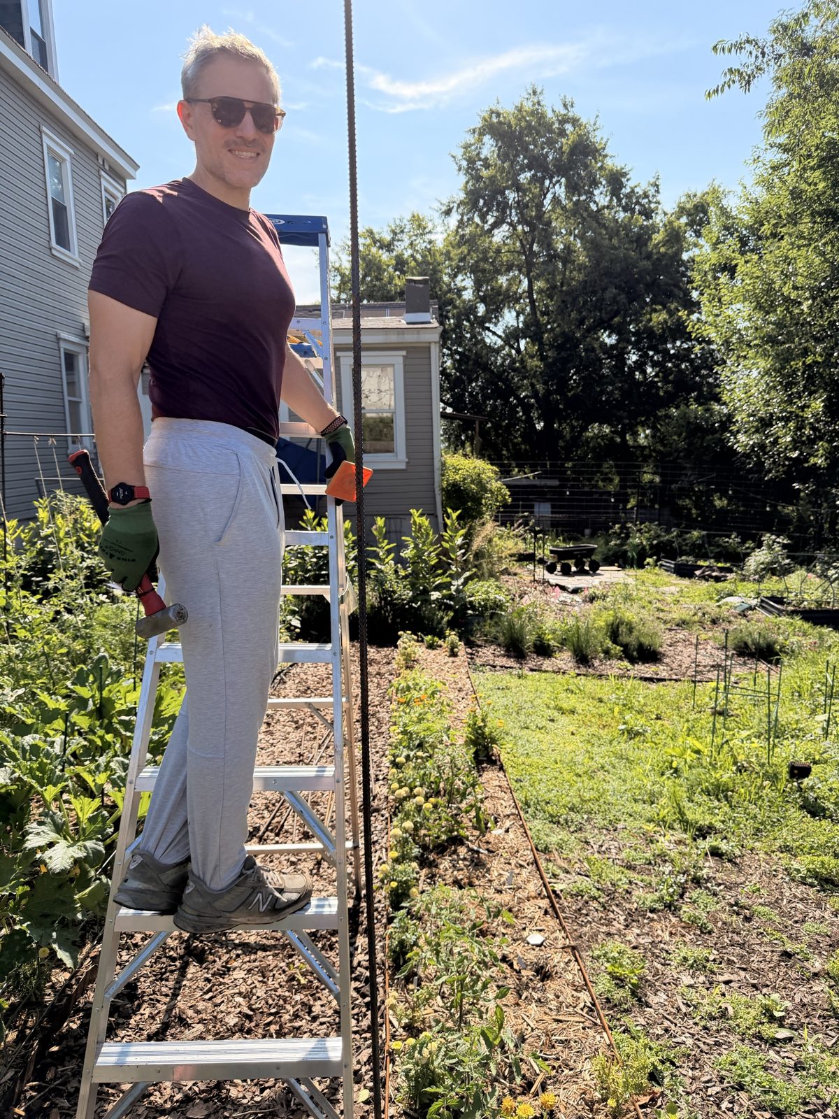 Michael on a stepladder in the garden with a hammer, next to a tall rebar post