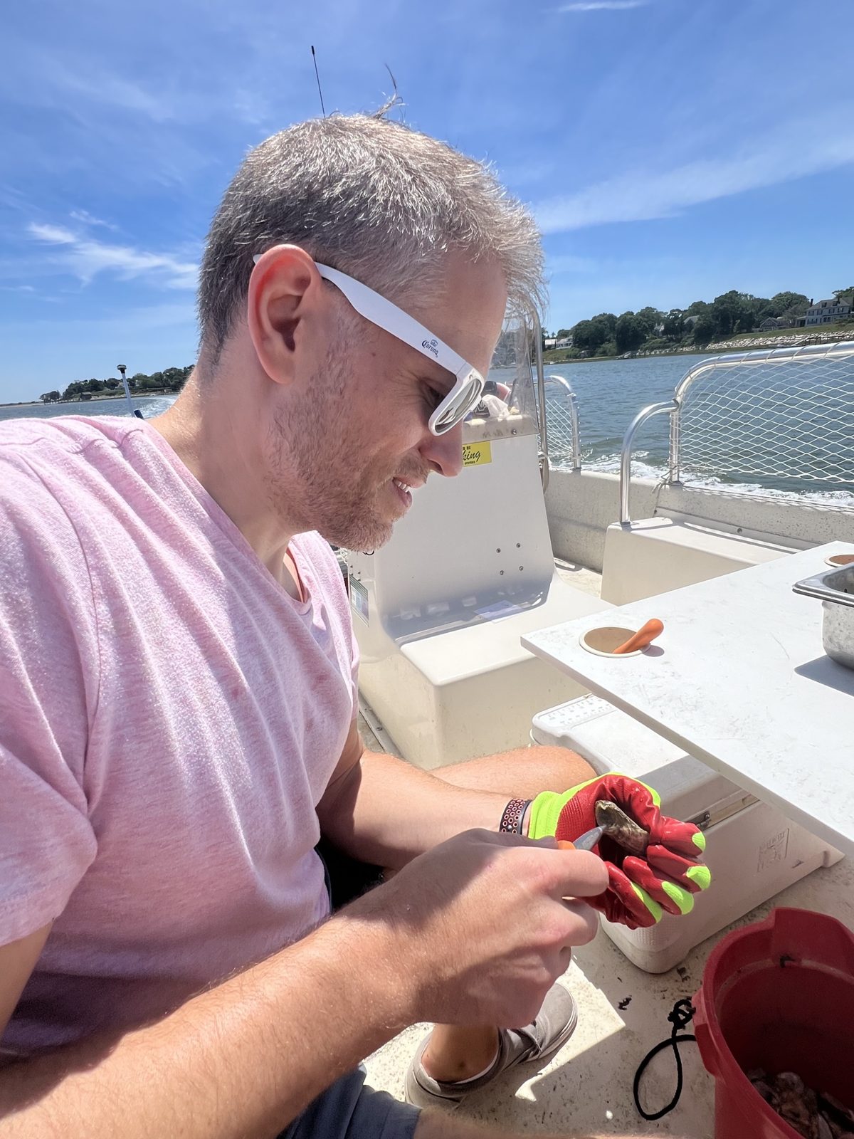 Michael in a work glove shucking an oyster on a boat out on the water